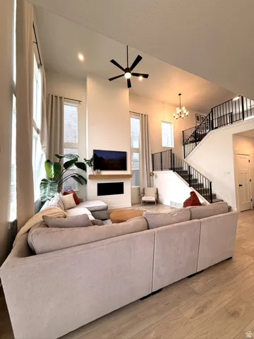 Two-story living area with high ceilings, wood-finish flooring, a built-in fireplace, and a contemporary ceiling fan