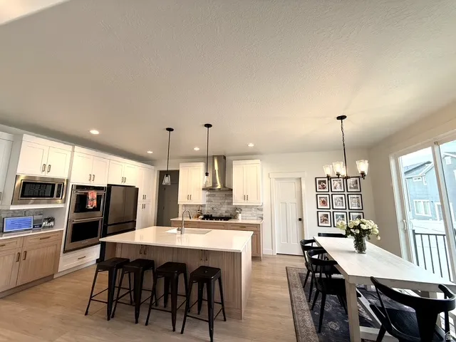 Kitchen featuring stainless steel appliances, a center island with seating, pendant lighting, and light wood-finish flooring