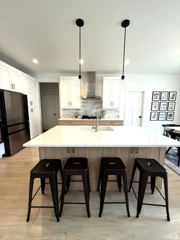 Spacious kitchen featuring a large island with a composite countertop, wood-finish flooring, white cabinetry, and stainless steel appliances