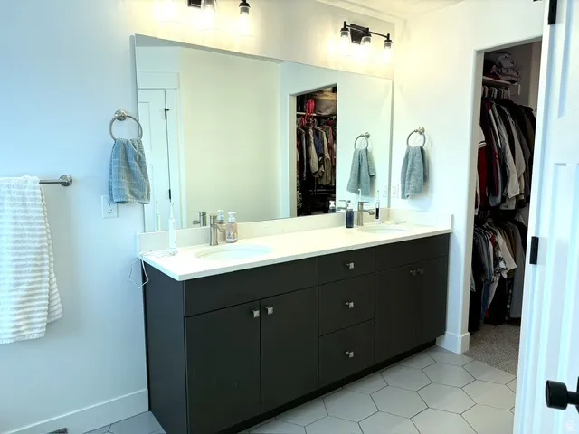 Double vanity with undermount sinks, white countertop, dark cabinetry with chrome hardware, and hexagonal floor tiling