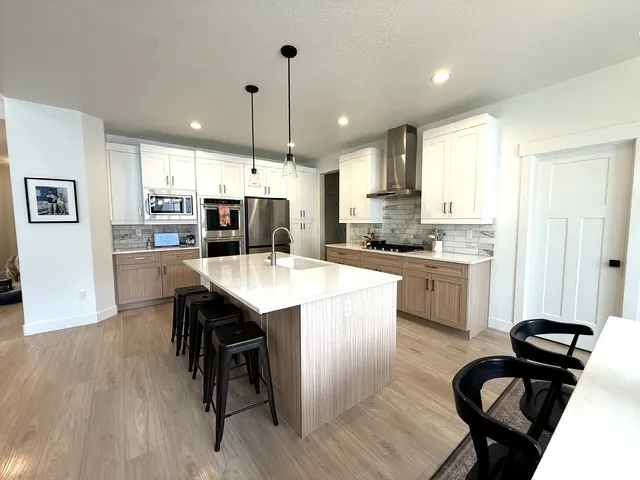 Kitchen featuring wood-finish flooring, two-tone cabinetry, a large center island with a sink, stainless steel appliances, and pendant lighting