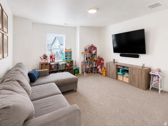 Carpeted room with a wall-mounted media console, a window with blinds, and recessed lighting