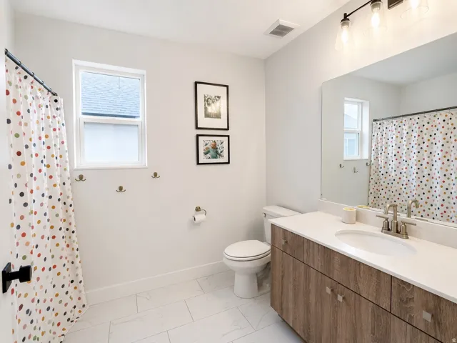 White tiled flooring, vanity with wood-finish cabinetry, white countertop, and a single window