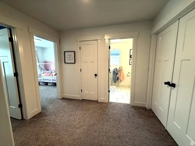 White shaker-style doors with matte black hardware, carpeted hallway, tiled bathroom flooring, and a window with natural light