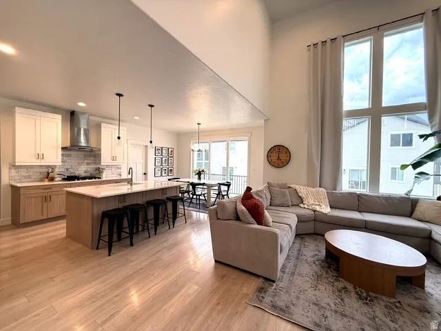 Open-concept living area with soaring ceilings, a full kitchen featuring a central island with bar seating, wood-finish flooring, and expansive windows