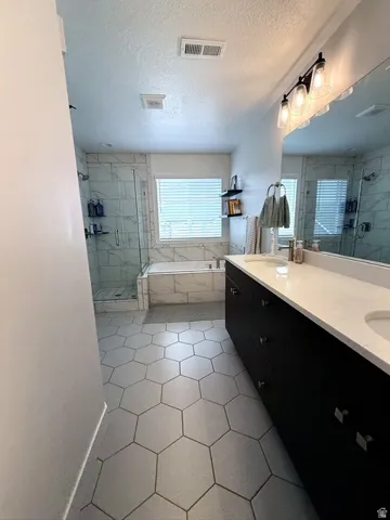 Dual vanity with light-toned countertops and dark cabinetry, a separate soaking tub, and a glass-enclosed shower
