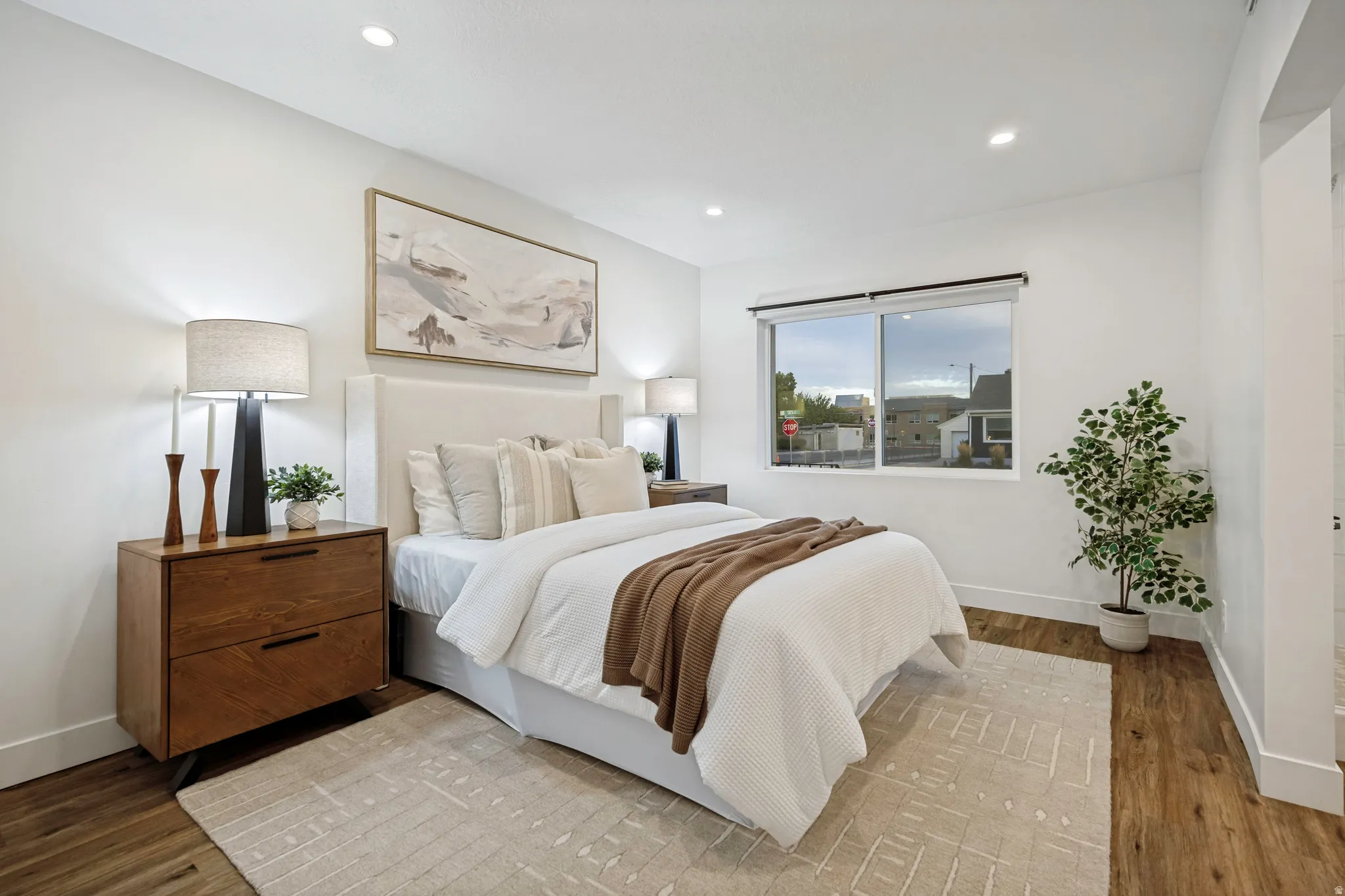 Recessed lighting, wood-finish flooring, white walls, and a large window with roller shades