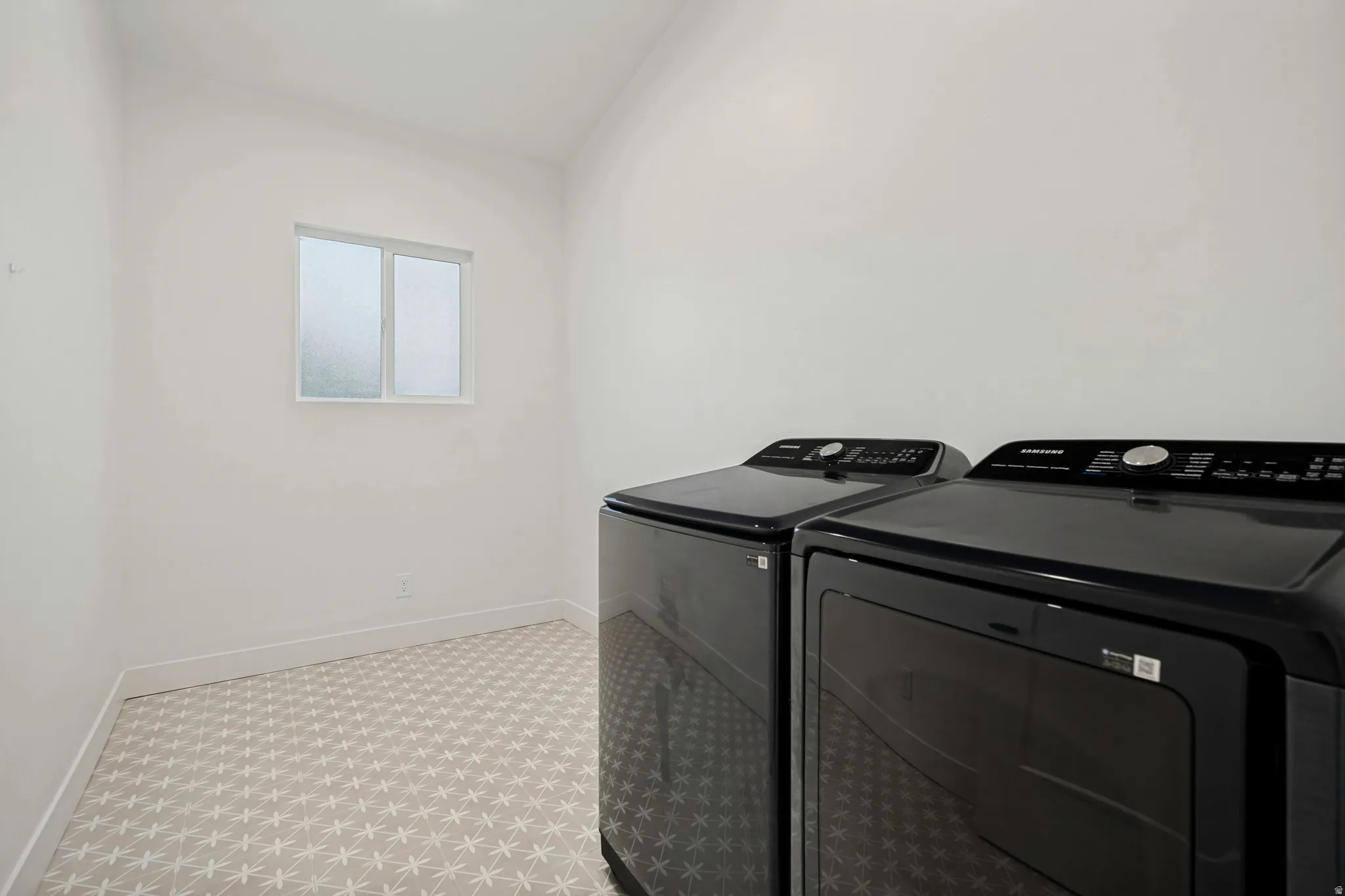 Dedicated laundry space featuring a window, patterned flooring, and a pair of dark-finished appliances