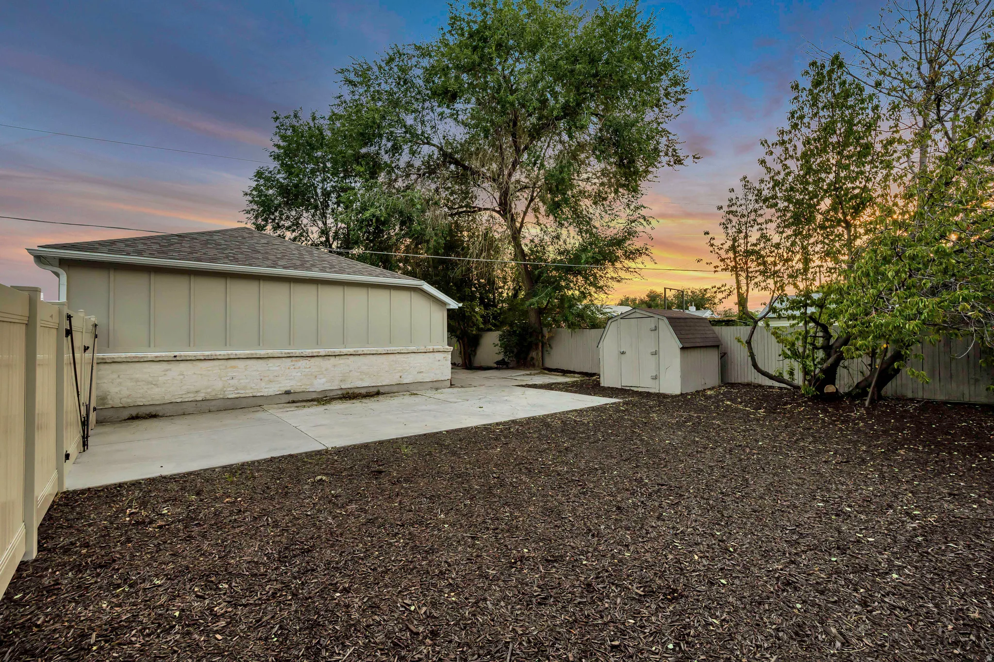 Expansive outdoor area featuring a concrete pad, a storage shed, and mature trees