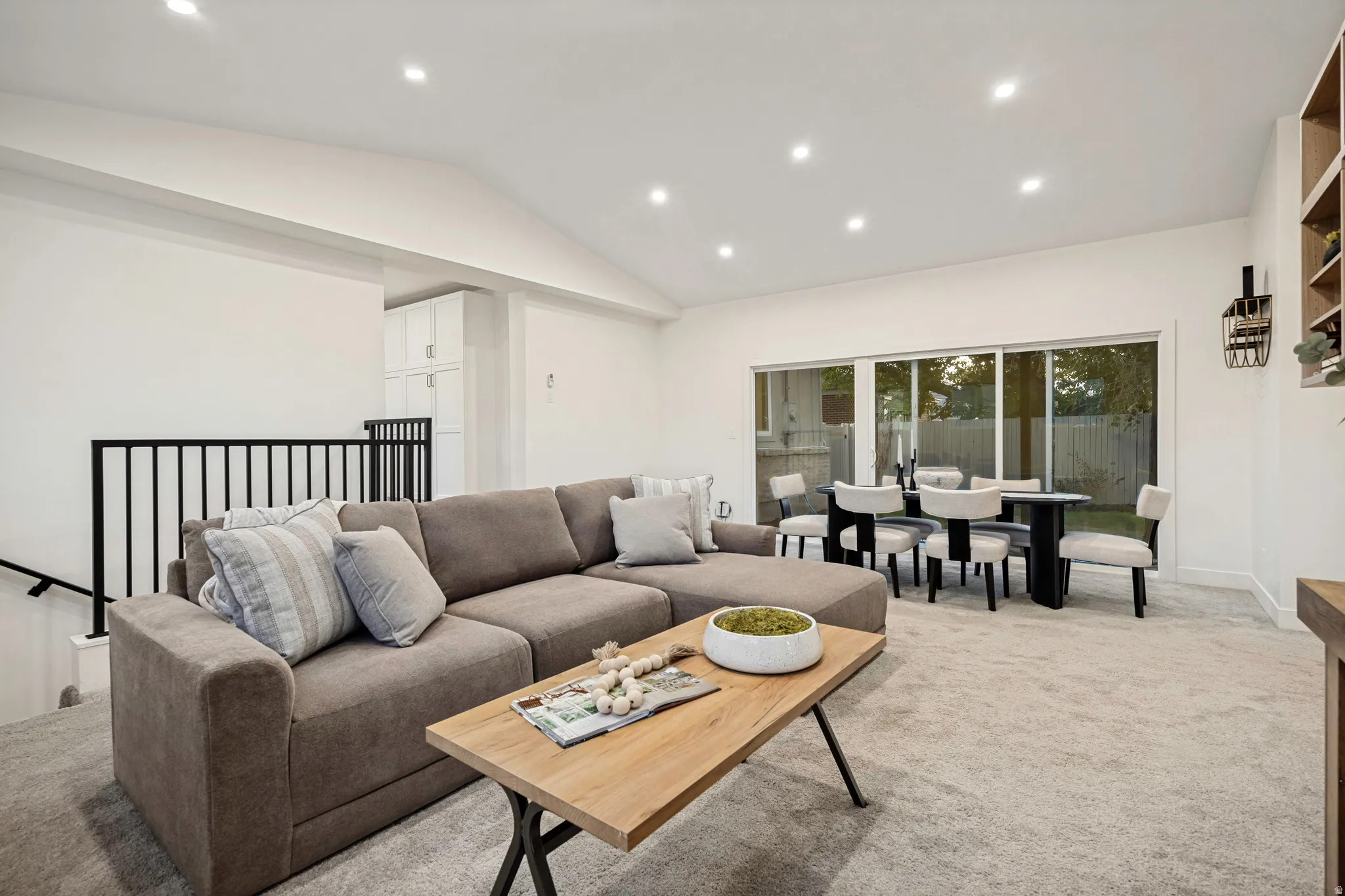 Vaulted ceiling with recessed lighting, black metal railing, and light-toned carpeting