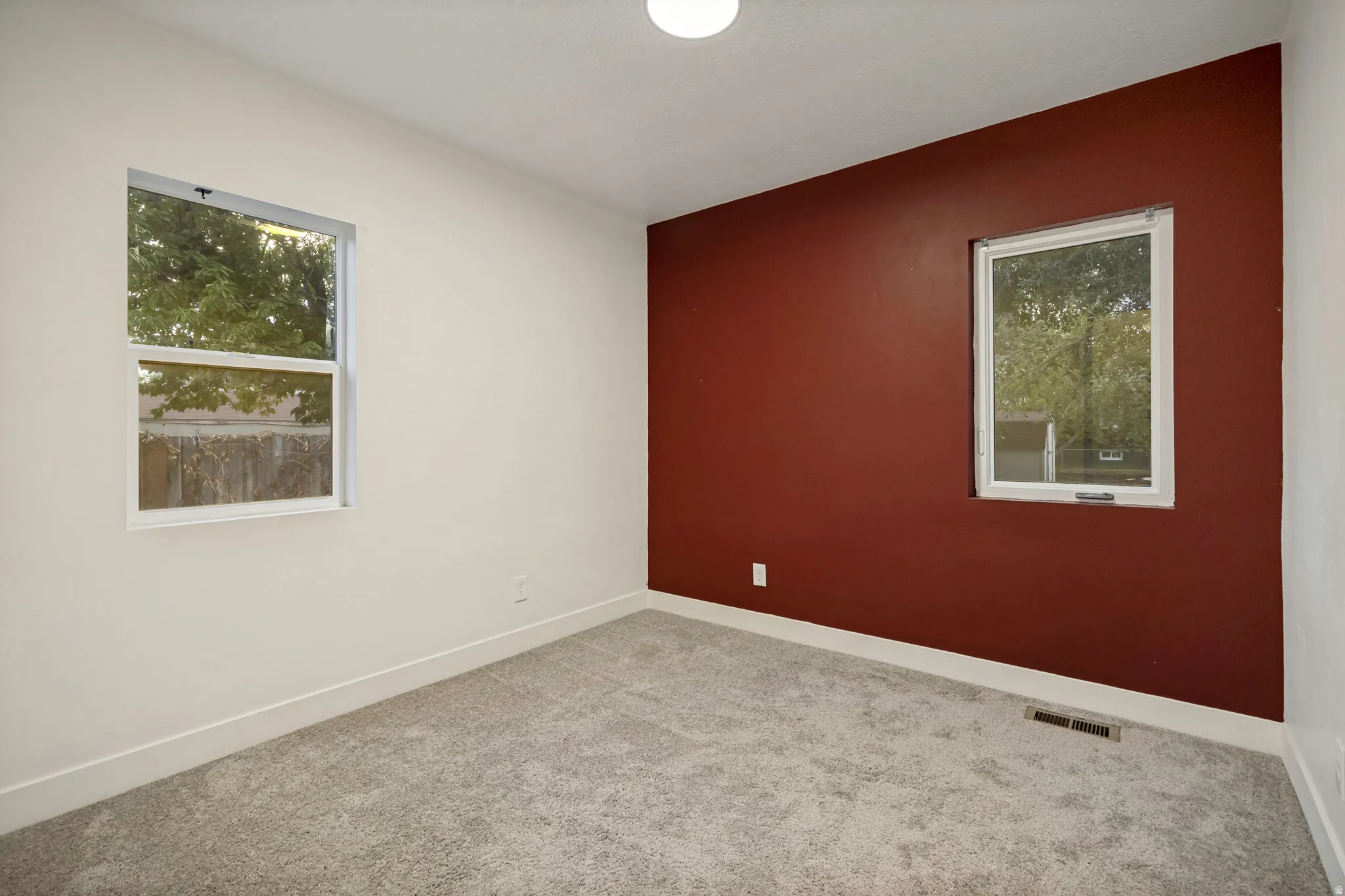 Neutral carpeting, two windows, and a red accent wall