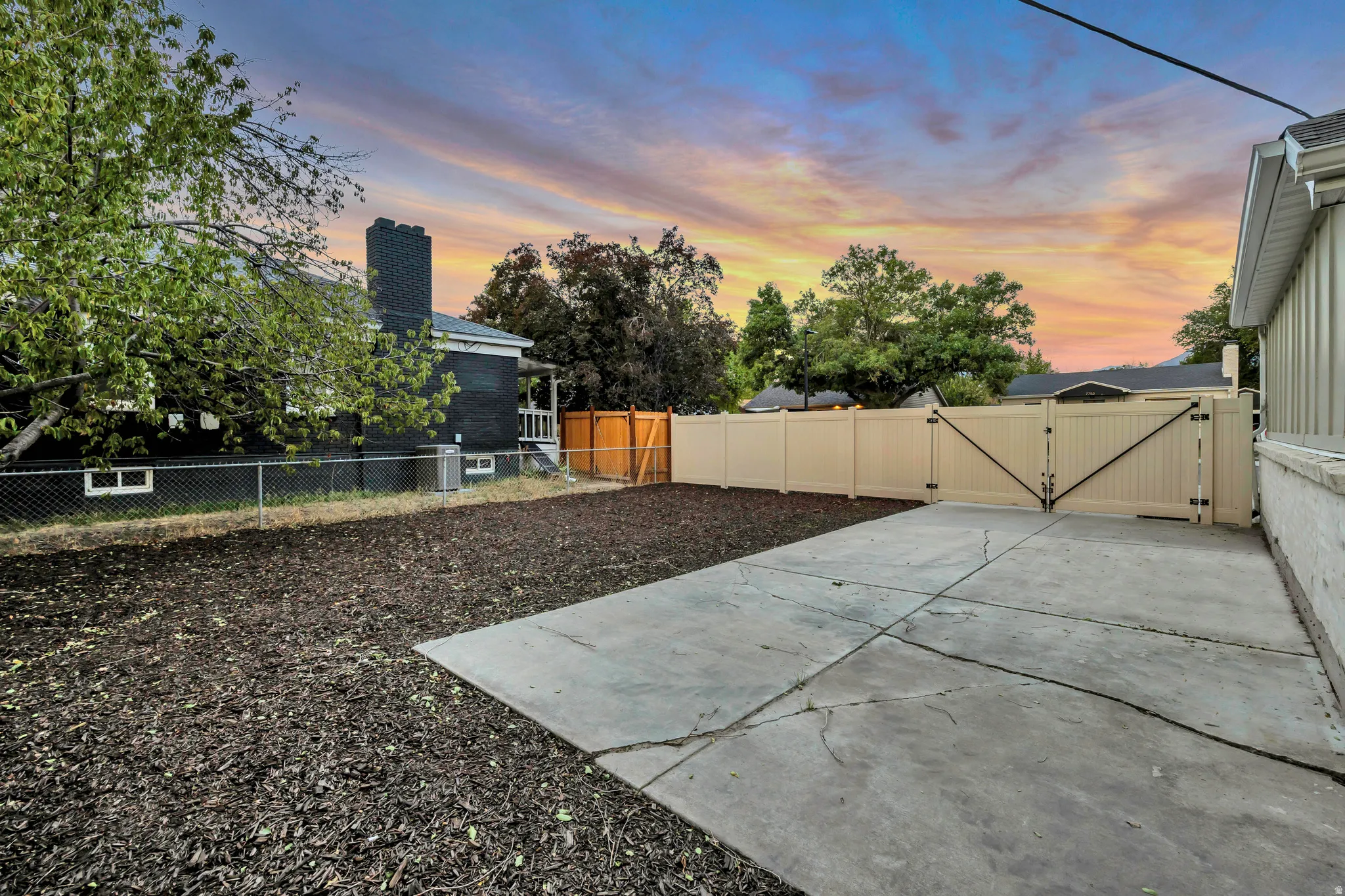 Expansive concrete patio with a large gate, bordered by a full-height privacy fence