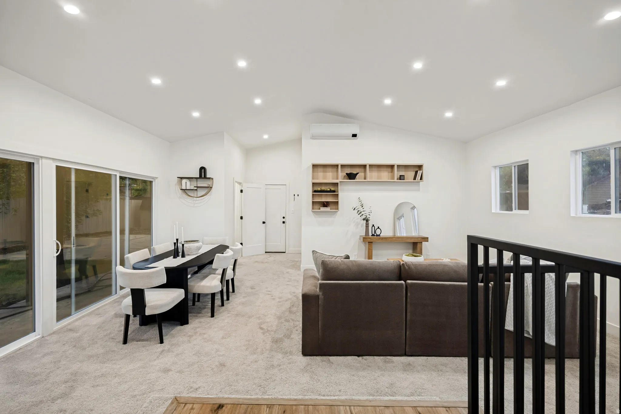 Vaulted ceilings with recessed lighting, sliding glass door, white walls, wood-finish flooring, and black metal railing