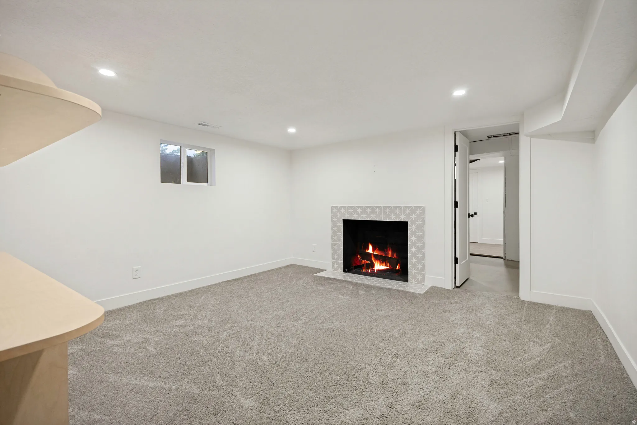 Recessed lighting, light gray carpet flooring, window with natural light, tiled fireplace surround, and a built-in countertop