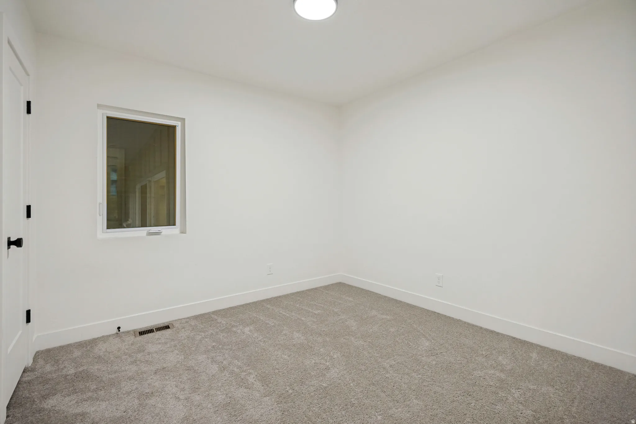 Neutral wall colors, white trim, grey carpet, and a single window