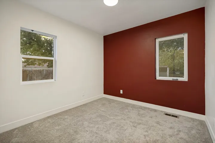 Neutral carpeting, two windows, and a red accent wall