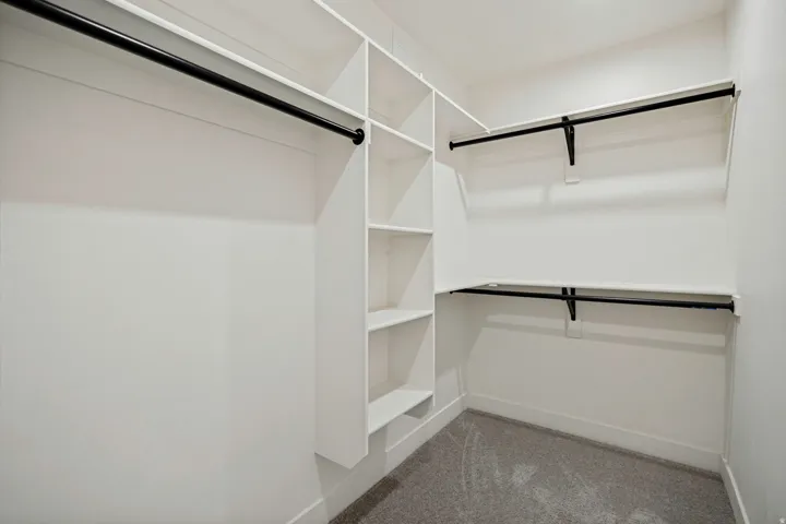 Built-in shelving, multiple hanging rods, and light-colored carpeting