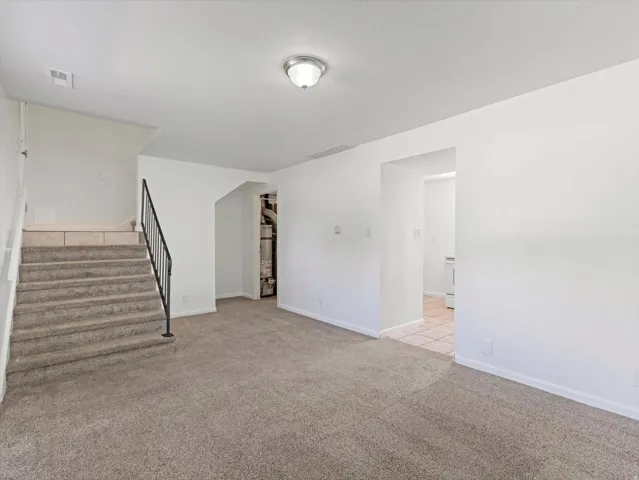 Carpeted flooring throughout, white walls, flush mount ceiling light, and staircase with black metal railing
