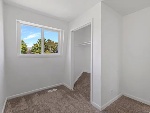 Neutral wall paint, window with exterior landscaping, wall-to-wall carpeting, and closet with built-in shelving