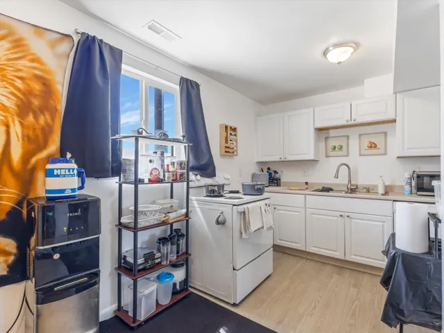 Kitchen featuring white cabinetry, light wood-finish flooring, a white range, and a window with natural light