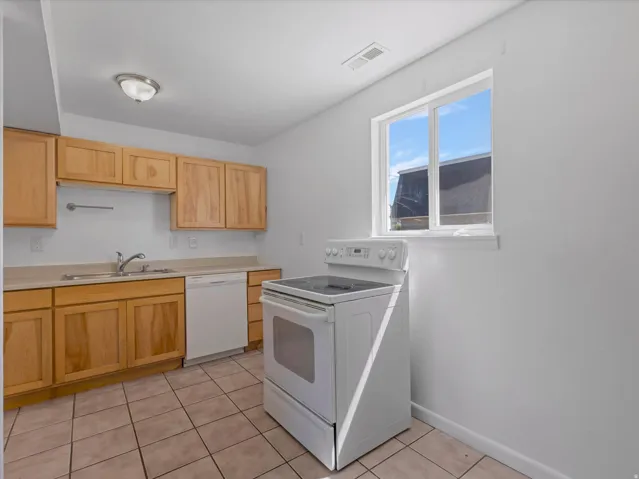 Kitchen featuring wood cabinetry, tiled flooring, white built-in dishwasher, white range, and a window