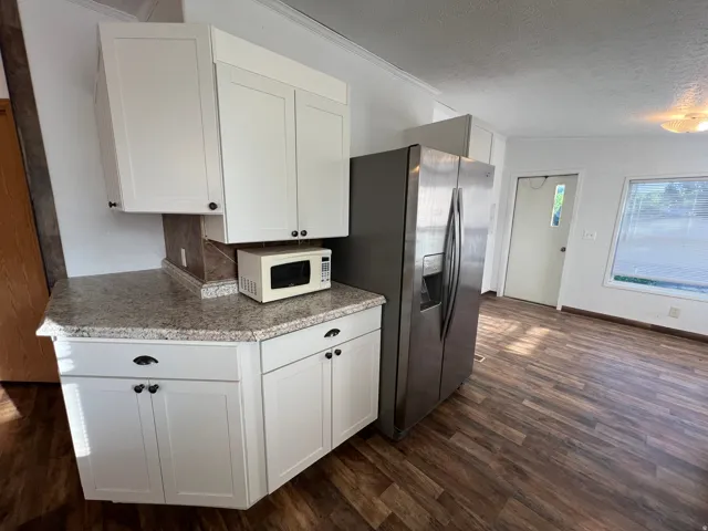 White cabinetry with dark hardware, stone-finish countertops, stainless steel refrigerator, and wood-finish flooring