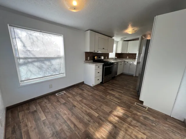 Kitchen featuring wood-finish flooring, white cabinetry, stainless steel appliances, and a tiled backsplash