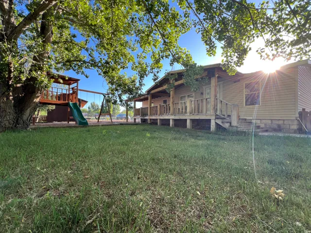 Spacious property featuring a large tree, a play structure with a slide, a swing set, and a home with a covered porch