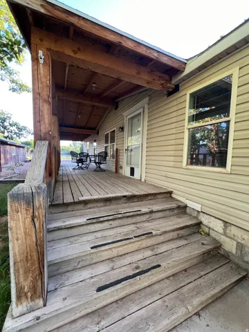 Covered wooden porch featuring exposed beam ceiling, wood plank flooring, and multiple windows