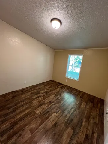 Wood-finish flooring with a varied plank pattern, light-toned wall finishes, and a single window with blinds