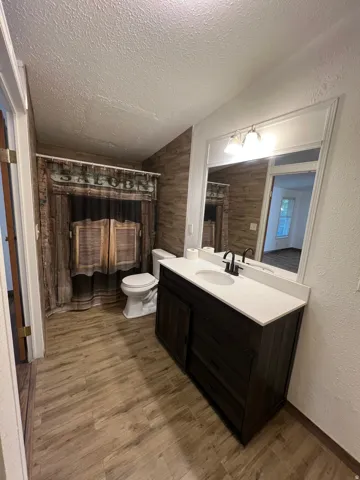 Wood-finish flooring, dark wood vanity with white countertop, integrated sink, and black-finish faucet
