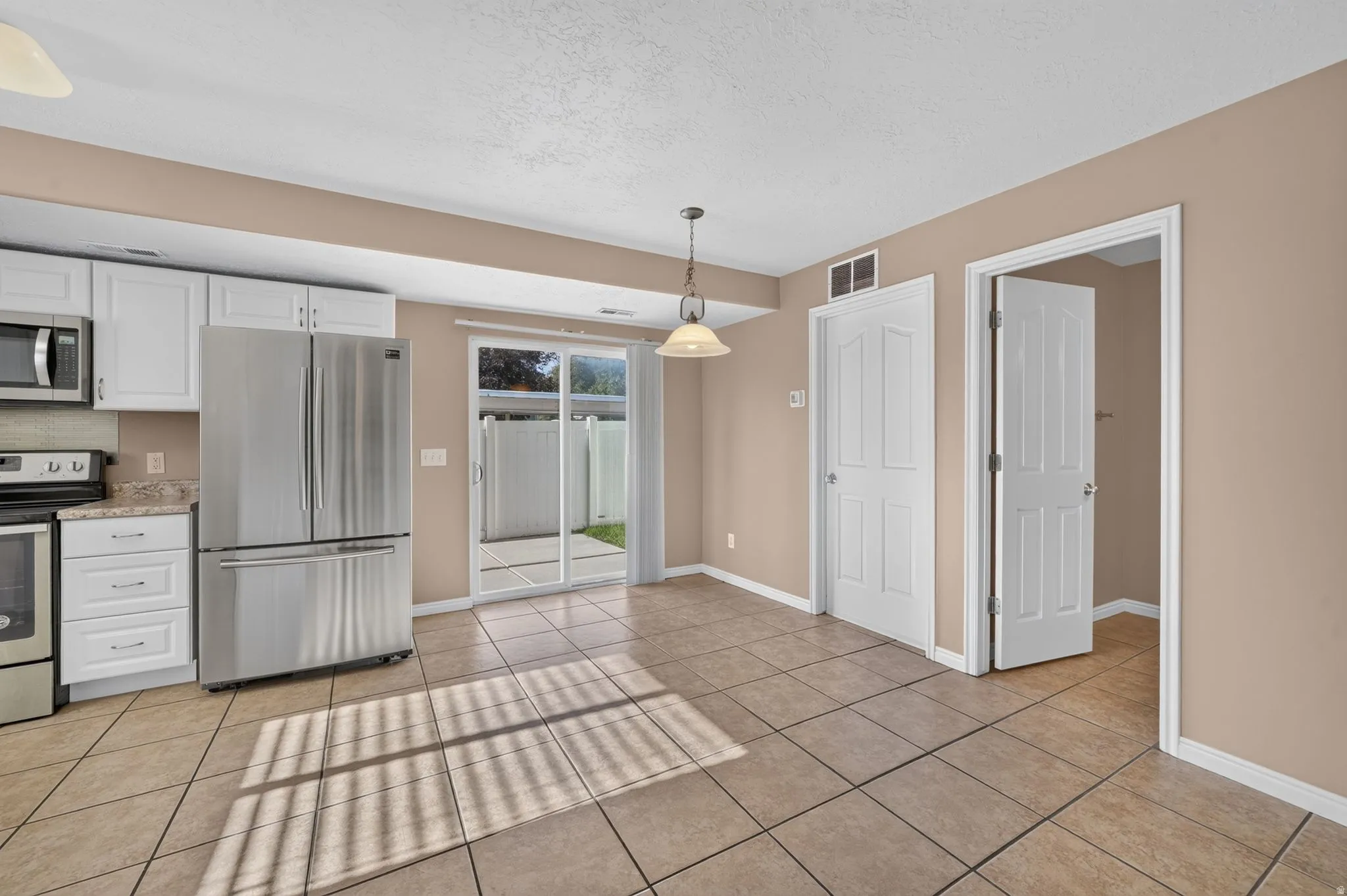 Kitchen with white cabinetry, stainless steel appliances, tile flooring, and sliding glass doors to a patio