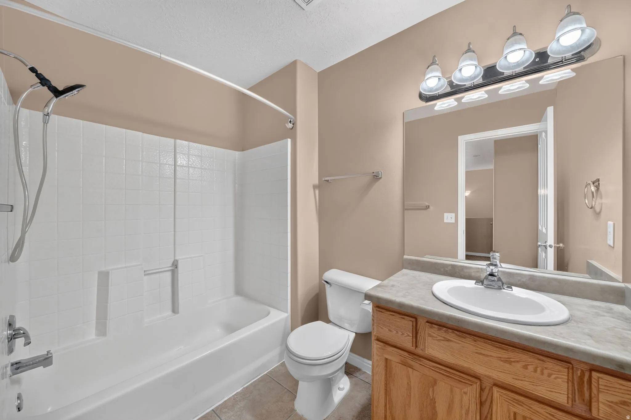Bathroom featuring a bathtub with a white tiled shower surround, a wood-finish vanity with an integrated sink, a large mirror, and a four-light fixture