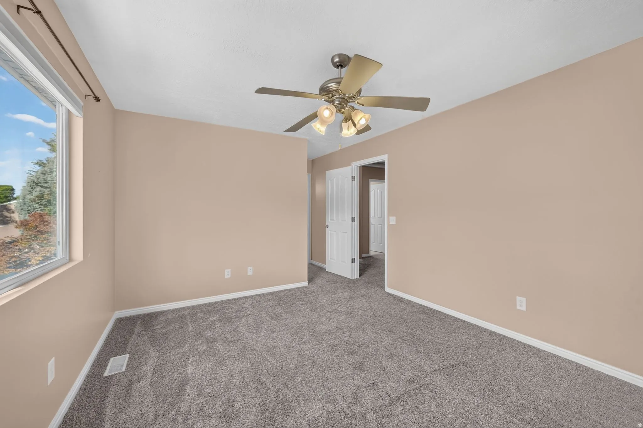 Wall-to-wall carpeting with light-toned walls, a large window, and a ceiling fan with integrated lighting