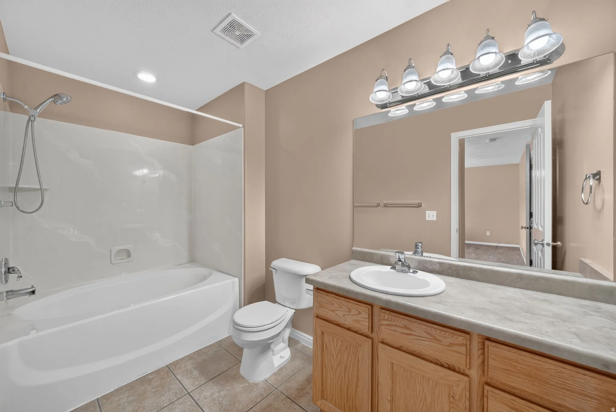 Full bathroom featuring a single vanity with wood cabinetry, a large mirror, a toilet, and a combination shower and tub with a white surround