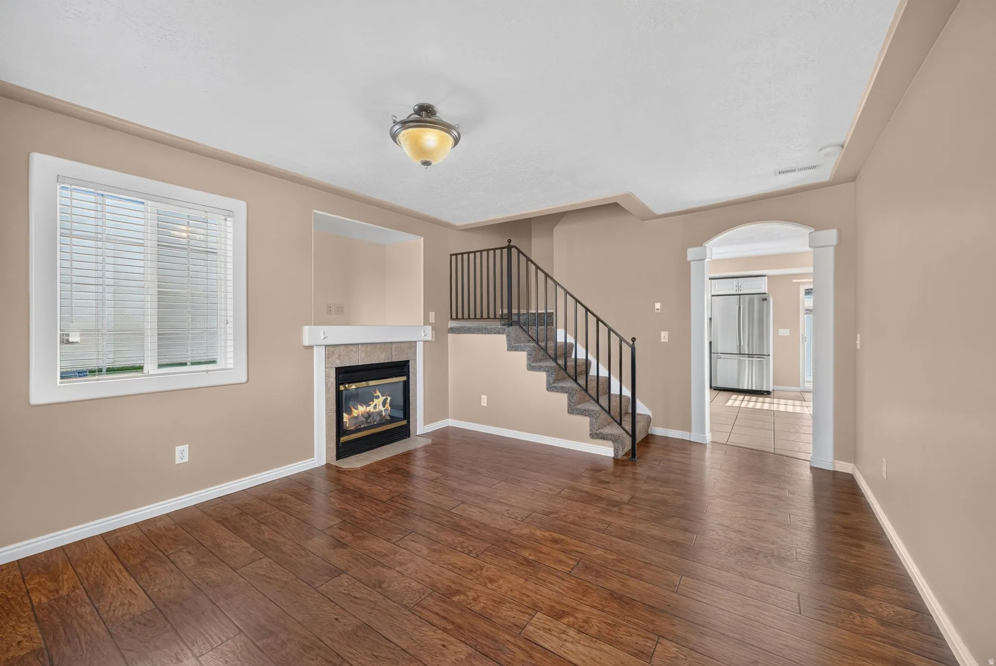 Wood-finish flooring with a fireplace, archway, and staircase featuring metal railings