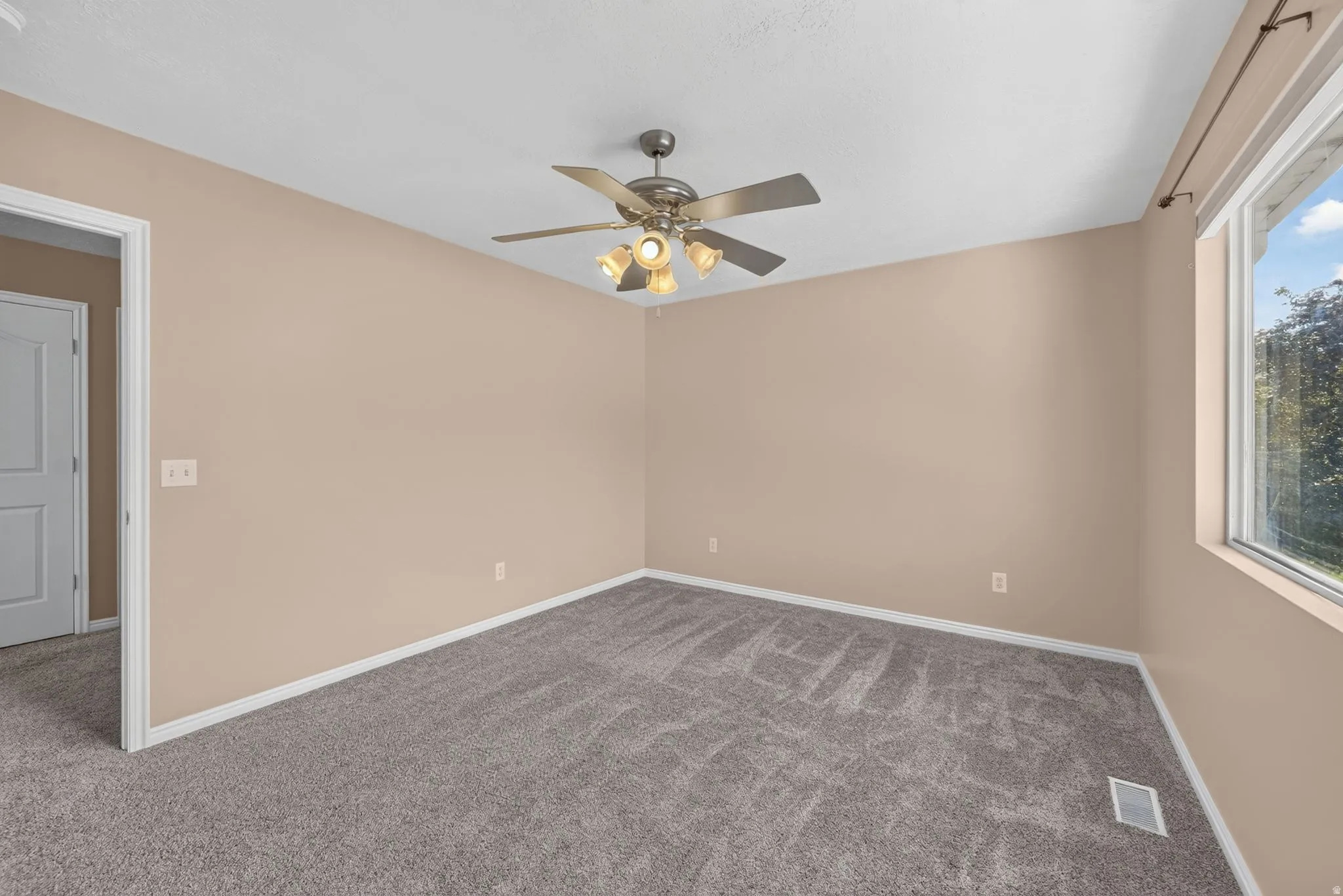 Spacious room featuring neutral carpeting, light-colored walls, a ceiling fan with integrated lighting, and a large window