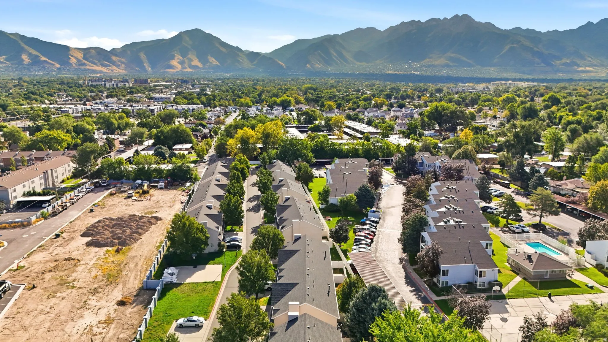 Community setting with residential buildings, mature trees, mountain backdrop, and an outdoor swimming pool