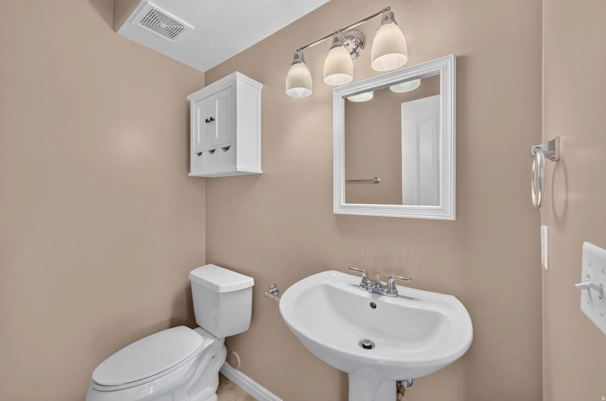 Pedestal sink with chrome fixtures, wall-mounted white framed mirror, and a three-light vanity fixture