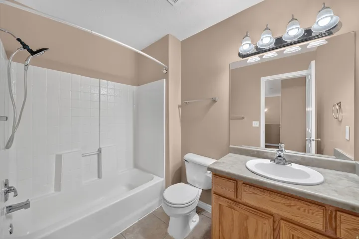 Bathroom featuring a bathtub with a white tiled shower surround, a wood-finish vanity with an integrated sink, a large mirror, and a four-light fixture
