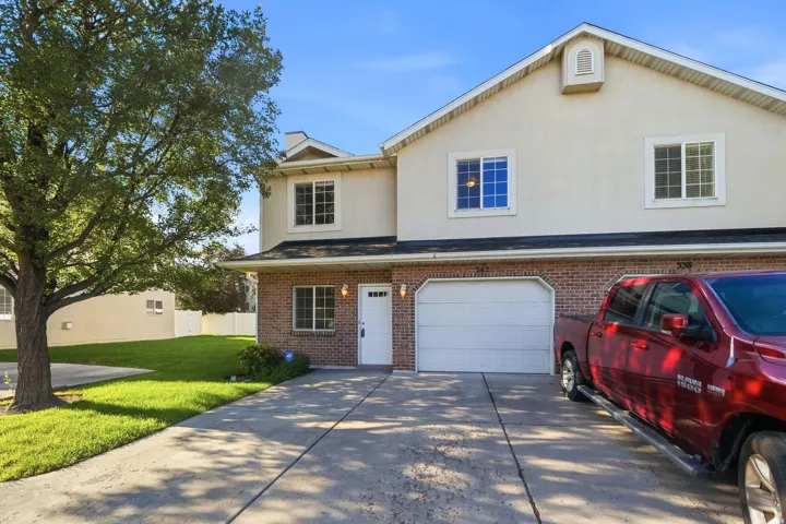 Brick and stucco exterior with an attached garage, paved driveway, and manicured lawn