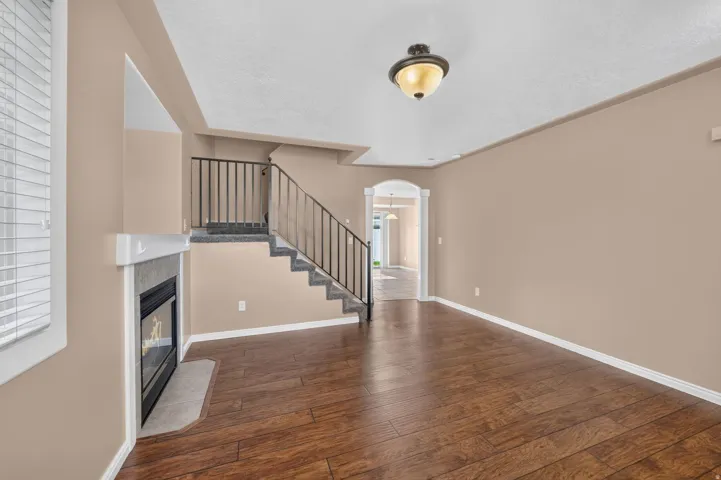 Wood-finish flooring, staircase with metal railings, built-in fireplace with hearth, arched doorway, and semi-flush mount ceiling light fixture