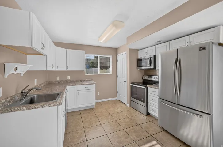 Kitchen featuring white cabinetry, stainless steel appliances, a double basin sink, ample counter space, and tile flooring