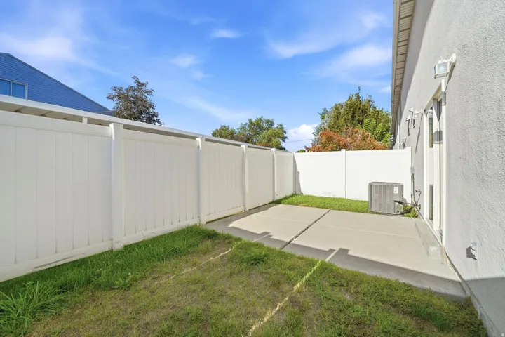 Private backyard featuring a concrete patio, exterior wall lighting, and a white vinyl privacy fence