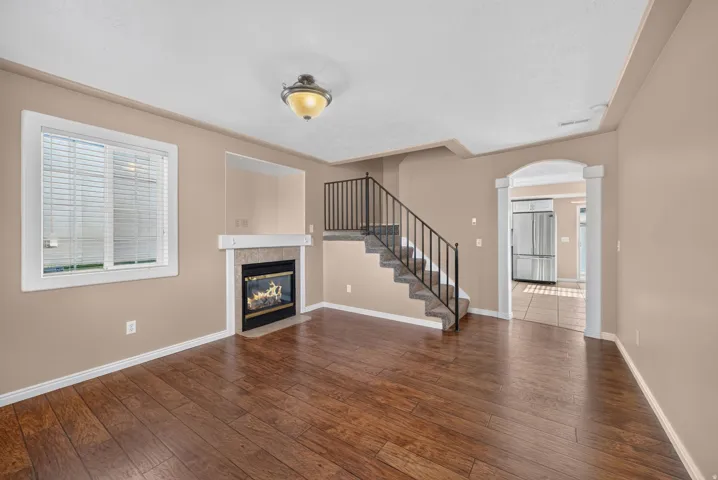 Wood-finish flooring with a fireplace, archway, and staircase featuring metal railings