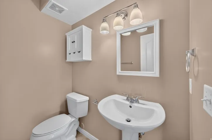 Pedestal sink with chrome fixtures, wall-mounted white framed mirror, and a three-light vanity fixture