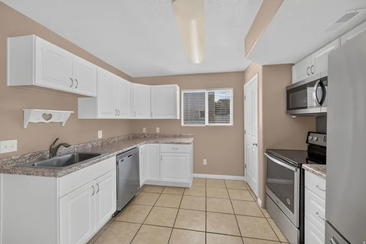 Kitchen featuring white cabinetry, stainless steel appliances, a double basin sink, and tile flooring
