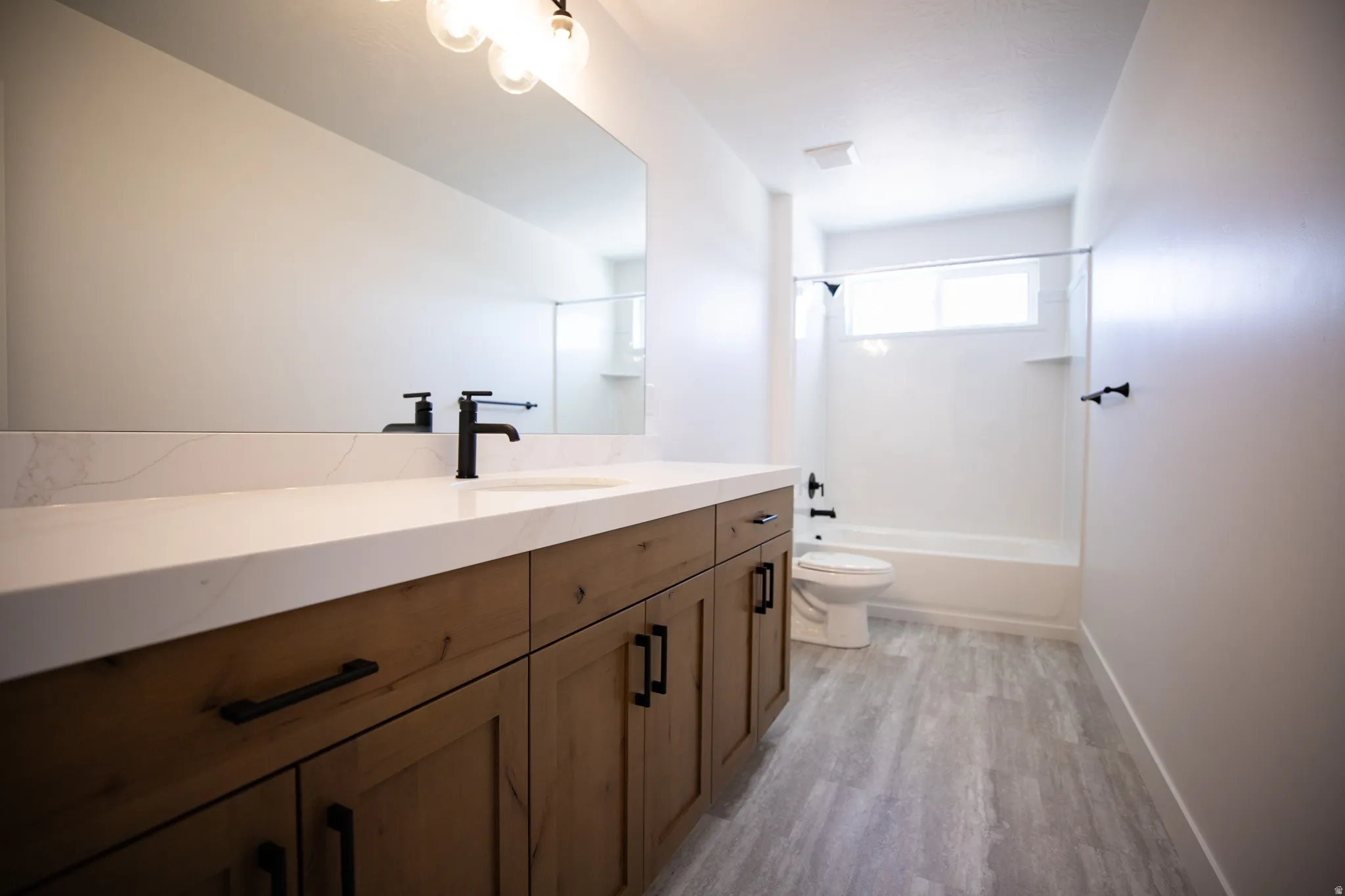 Full secondary bath with extra-long vanity, stained wood cabinets and quartz slab countertop.