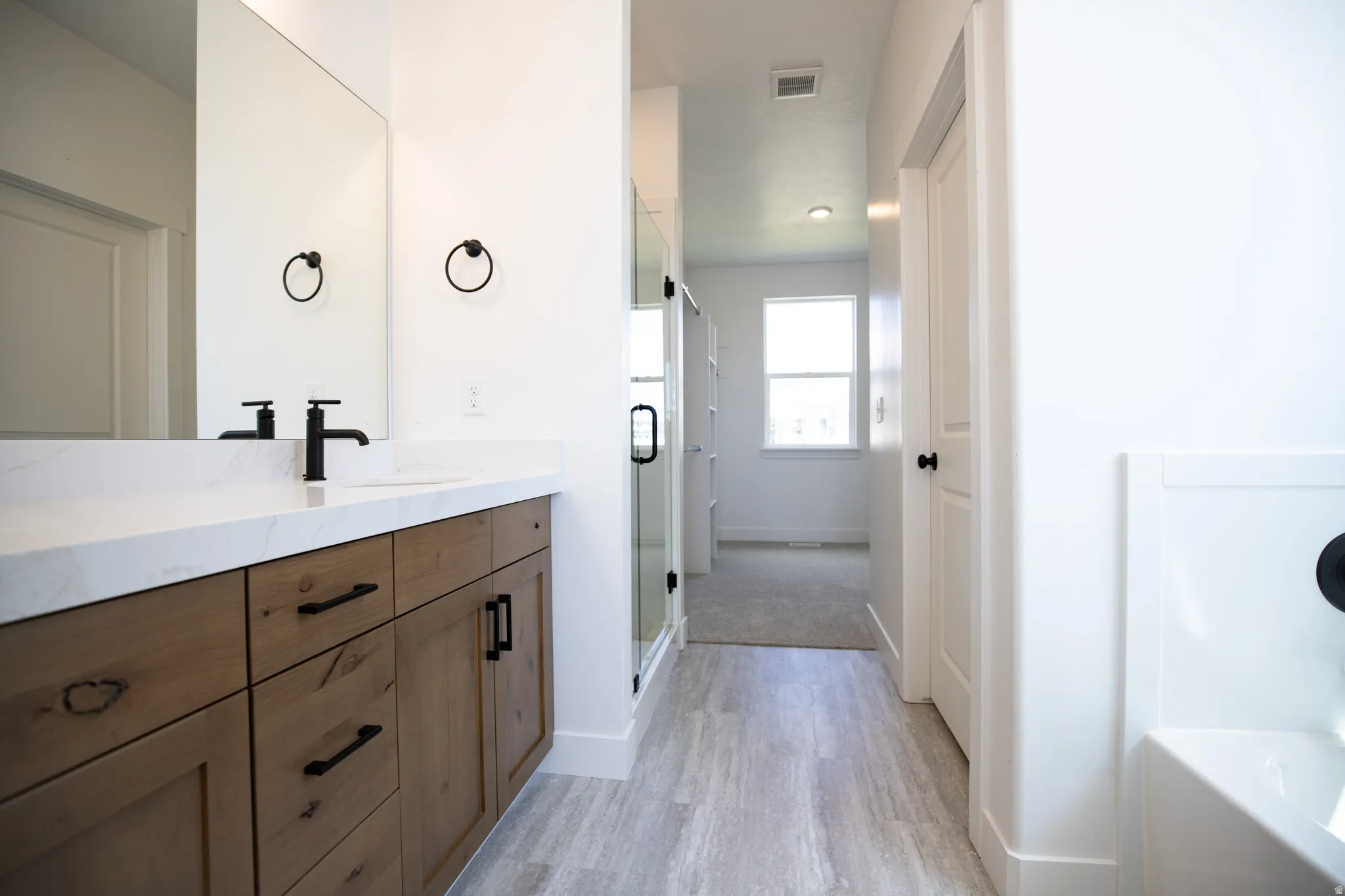 Primary bath on main level with dual sinks, stained wood cabinets, quartz slab countertops, soaker tub and walk-in Euro shower.