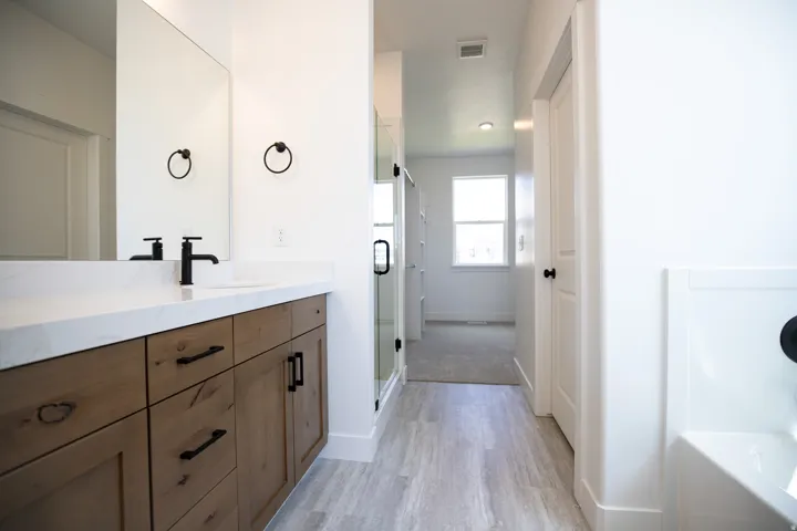 Primary bath on main level with dual sinks, stained wood cabinets, quartz slab countertops, soaker tub and walk-in Euro shower.